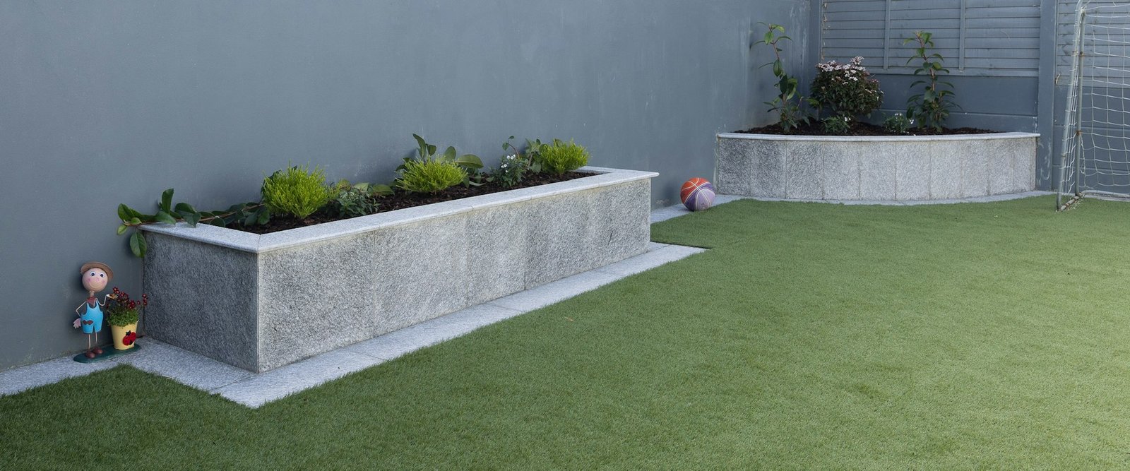 Artificial grass lawn installed in a backyard with raised stone planters