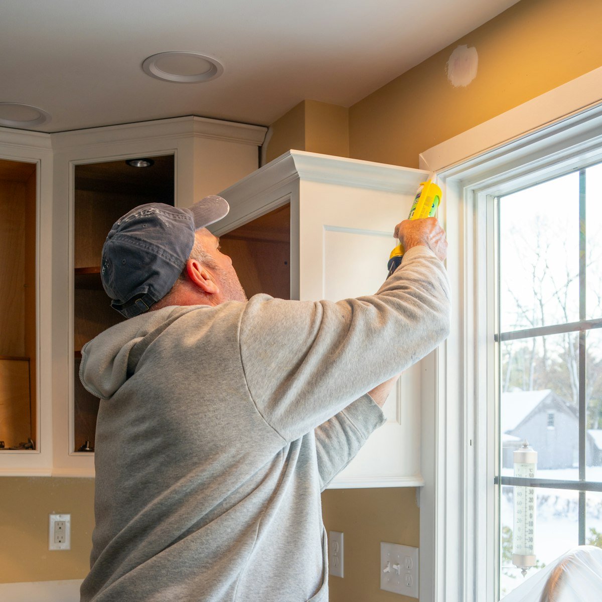 Handyman caulking the trim between a kitchen cabinet and a window frame