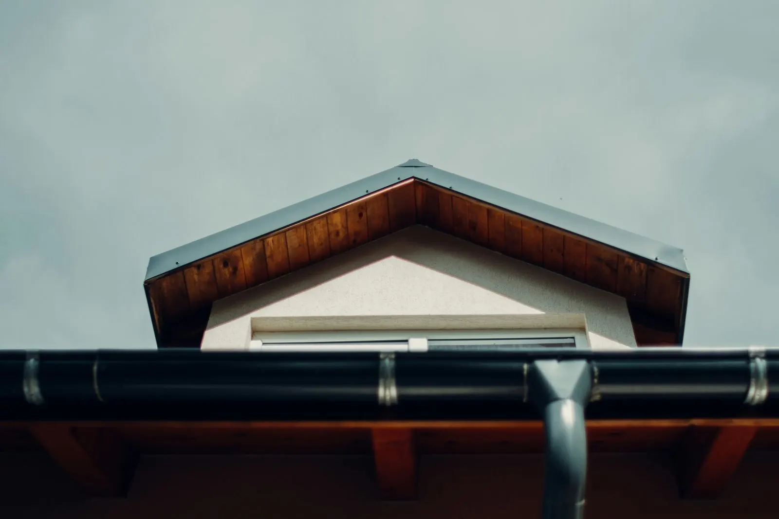 Clean black rain gutter and metal downspout under a gable with wooden eaves